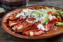 Enchiladas potosinas de masa rojiza con chile, queso, crema, aguacate y vegetales en plato de barro