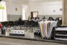Mostrador de atención pública con documentos, turnos numerados y una sala comunitaria al fondo, imagen editorial sobre gobernabilidad.