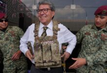 Ricardo Monreal prueba un chaleco táctico acompañado de dos militares durante una exhibición.