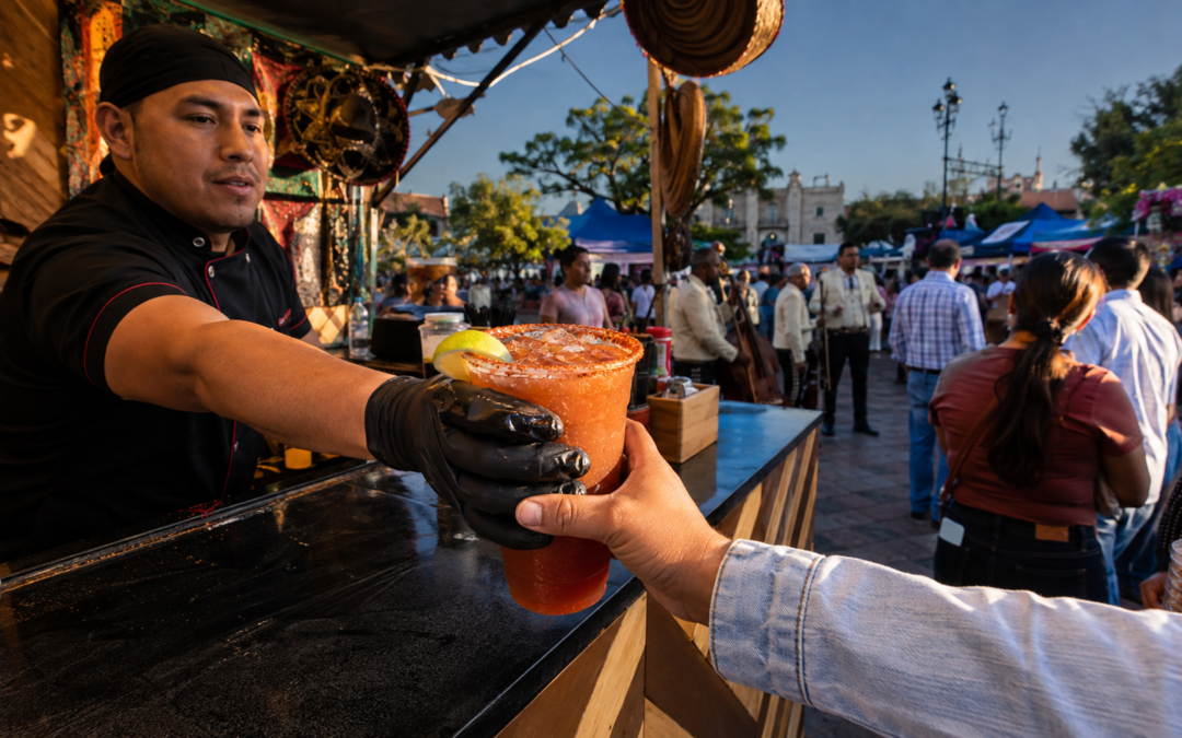 Vaso de michelada escarchado en una plaza de Villagrán, con puestos de comida, música y visitantes en una escena documental mexicana.