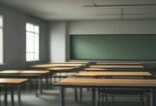 Salón de clases vacío con pupitres de madera alineados, pizarrón verde al fondo y luz natural que entra por las ventanas