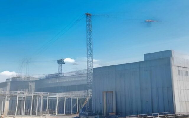 Obra de una gran nave industrial en construcción con estructura metálica, una grúa torre y cielo azul despejado