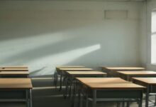 Salón de clases vacío con mesas y sillas de madera alineadas y luz de la mañana que entra por una ventana e ilumina la pared
