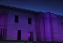 Fachada de un edificio de piedra iluminada con luz morada durante la noche
