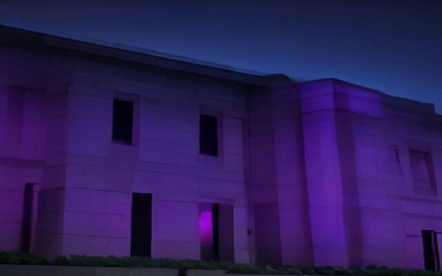Fachada de un edificio de piedra iluminada con luz morada durante la noche
