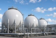 Tanques esféricos blancos de almacenamiento de gas y tuberías de acero en una terminal industrial bajo cielo azul, sin personas