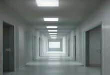 Pasillo largo de hospital con paredes blancas, puertas a ambos lados, piso brillante y lámparas de techo encendidas, sin personas