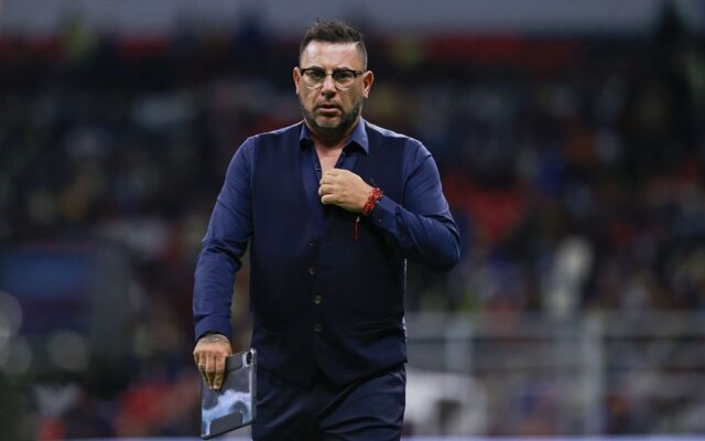 Antonio Mohamed, con chaleco azul marino, sostiene una tableta en la cancha