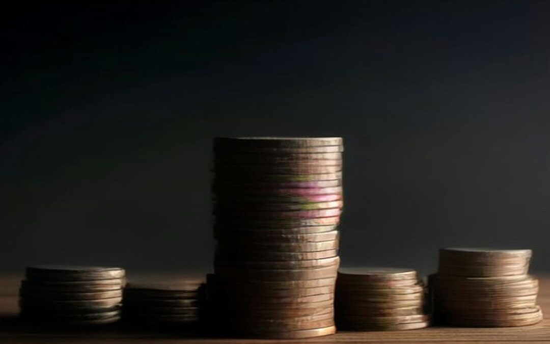 Torres de monedas metálicas de distintas alturas sobre una mesa de madera oscura iluminadas con luz lateral