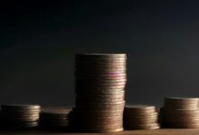 Torres de monedas metálicas de distintas alturas sobre una mesa de madera oscura iluminadas con luz lateral