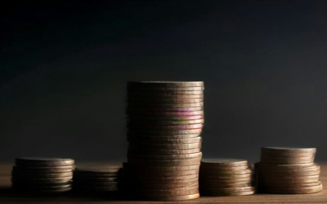 Torres de monedas metálicas de distintas alturas sobre una mesa de madera oscura iluminadas con luz lateral