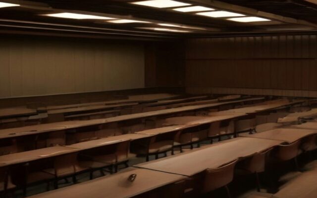 Salón legislativo vacío con filas de escritorios de madera y asientos alineados bajo una iluminación cálida en el techo