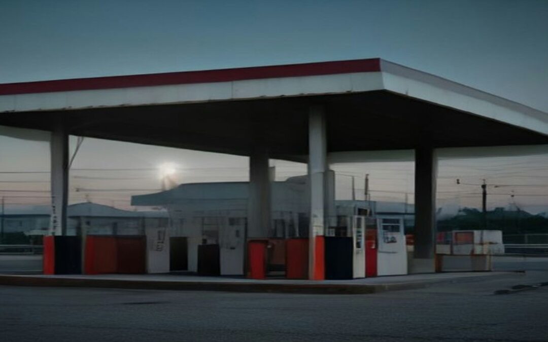 Estación de servicio vacía al atardecer, con bombas de combustible bajo un techo amplio y luz suave en el cielo