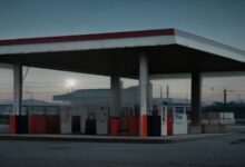 Estación de servicio vacía al atardecer, con bombas de combustible bajo un techo amplio y luz suave en el cielo
