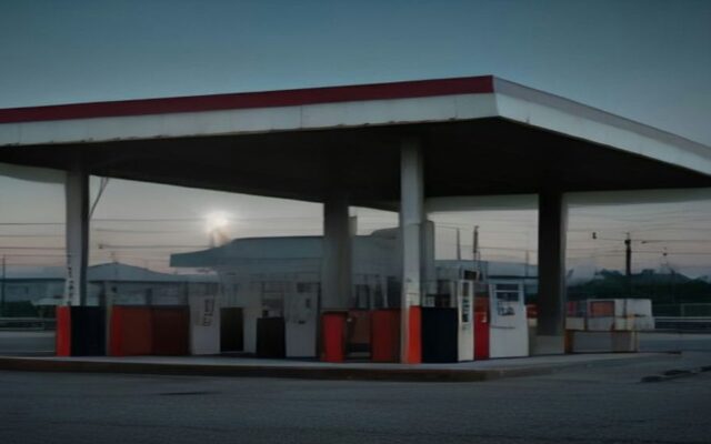 Estación de servicio vacía al atardecer, con bombas de combustible bajo un techo amplio y luz suave en el cielo