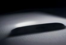 Silueta desenfocada de un teléfono celular sobre una superficie clara en penumbra, iluminada por un haz de luz lateral