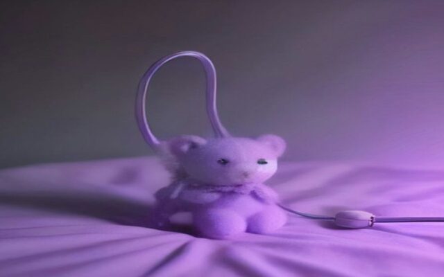 Oso de peluche morado sobre una manta lila, con un cable de estetoscopio a un lado y fondo desenfocado