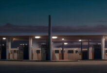 Estación de servicio vacía al anochecer con varias bombas de combustible iluminadas bajo un techo y un poste alto al centro