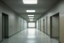 Pasillo largo de un edificio con piso brillante, puertas grises a ambos lados y lámparas fluorescentes en el techo