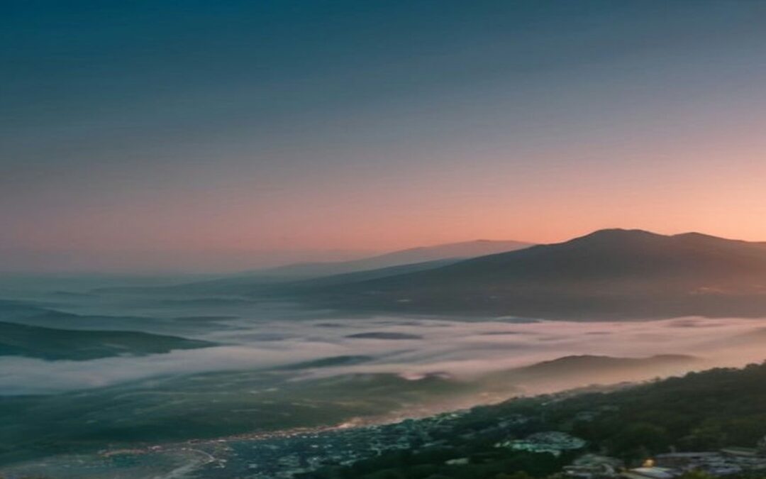 Valle con niebla al atardecer y un poblado que se extiende por la ladera de los cerros