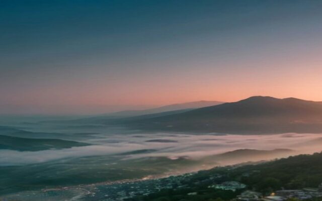 Valle con niebla al atardecer y un poblado que se extiende por la ladera de los cerros