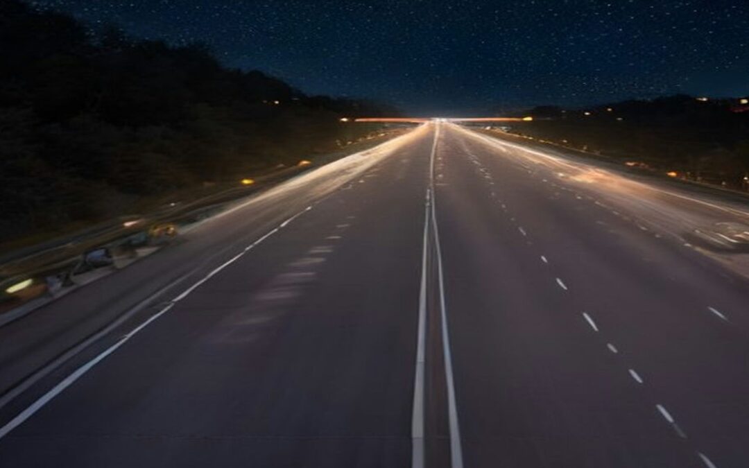 Vía rápida de varios carriles vacía al anochecer, con líneas blancas en el asfalto y luces de la ciudad en el horizonte