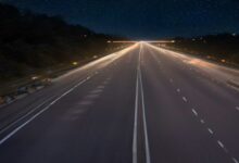 Vía rápida de varios carriles vacía al anochecer, con líneas blancas en el asfalto y luces de la ciudad en el horizonte